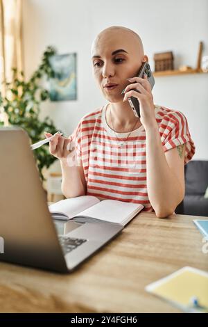 A young bald woman engages in a phone conversation while multitasking at her desk. Stock Photo