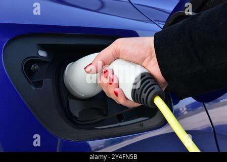 Woman charging an electric car with power supply cable. Stock Photo