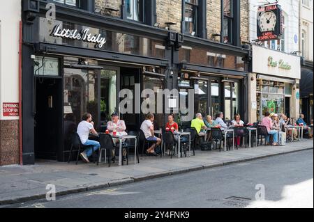 People enjoying food and drink seated at pavement tables outside Bar Italia coffee shop and Little Italy Italian restaurant Frith Street Soho London U Stock Photo