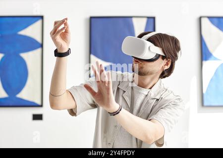 Minimal portrait of man wearing VR headset in modern art museum and while interacting with invisible digital artwork, copy space Stock Photo