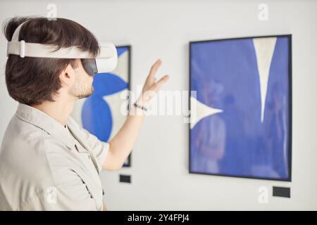 Back view of man wearing Vr in modern art show enjoying interactive mixed reality with paintings, copy space Stock Photo