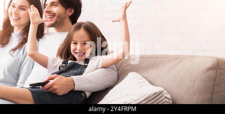 Joyful Little Girl Raising Hands And Smiling Next To Parents Stock Photo