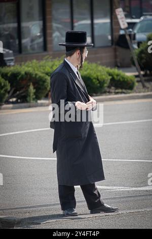 An orthodox young man with long curly peyus sticks his thumb out to hitchhike a ride in a mostly Jewish neighborhood in Rockland County, New York. Stock Photo