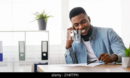 African businessman talking with companion on phone and checking financial reports Stock Photo