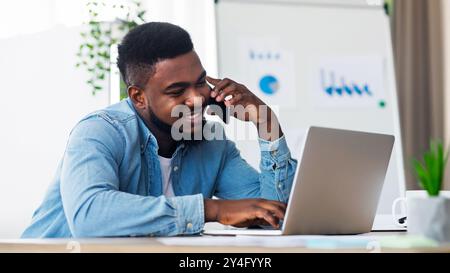 Employee talking on cellphone and working on laptop in office Stock Photo