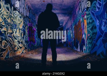 A person with a flashlight at night in in a graffiti-smeared tunnel, creepy, abstract, creative photo, colorful, blur, dark Stock Photo