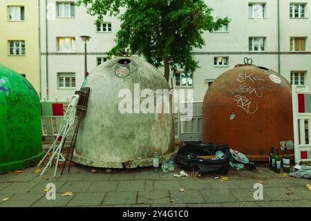 Round glass containers standing on a sidewalk with garbage lying around them Stock Photo