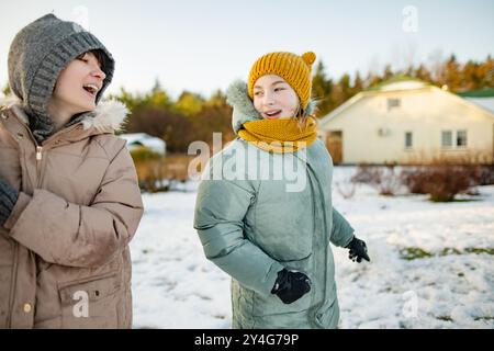 Adorable teenage girls building a snowman in the backyard. Cute children playing in a snow. Fun winter activities for family with kids. Stock Photo