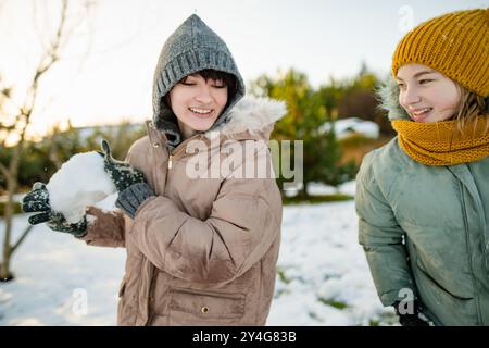 Adorable teenage girls building a snowman in the backyard. Cute children playing in a snow. Fun winter activities for family with kids. Stock Photo