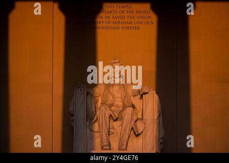 WASHINGTON DC, United States — The statue of Abraham Lincoln inside the Lincoln Memorial is illuminated by natural golden sunlight just after sunrise. This lighting effect, visible around the spring and fall equinox, enhances the monument's grandeur as the sun shines through the eastern entrance. The Lincoln Memorial, located on the National Mall, is one of the most iconic monuments in the United States. NB: The color and lighting are natural. Stock Photo