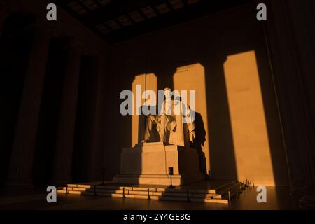 Lincoln Memorial Golden Sunrise Light Interior | WASHINGTON D.C., United States — A wide interior view frames Daniel Chester French's seated marble Lincoln beneath the carved dedication inscription, amber sunlight streaming through the Lincoln Memorial's eastern entrance and casting sharp column shadows across the chamber floor. The open-air portico is aligned precisely east-west, so near the equinoxes the low morning sun penetrates deep enough to illuminate the 19-foot (5.8 m) figure, a phenomenon that draws photographers only twice a year. Stock Photo