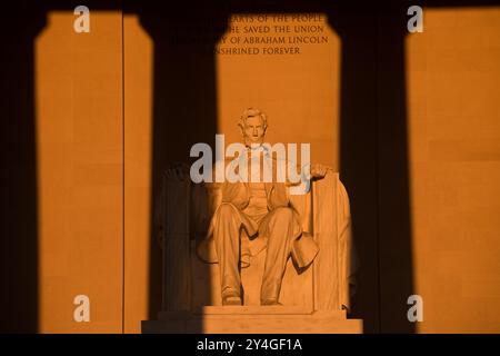 WASHINGTON DC, United States — The statue of Abraham Lincoln inside the Lincoln Memorial is illuminated by natural golden sunlight just after sunrise. This lighting effect, visible around the spring and fall equinox, enhances the monument's grandeur as the sun shines through the eastern entrance. The Lincoln Memorial, located on the National Mall, is one of the most iconic monuments in the United States. NB: The color and lighting are natural. Stock Photo