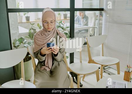 Muslim Woman Sitting in Modern Office Using Smartphone Stock Photo