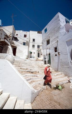 A woman walks down the steps of a charming whitewashed alley in Tetouans historic Medina, showcasing the vibrant local architecture. Stock Photo