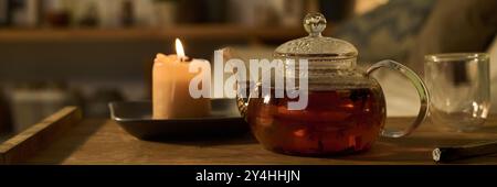 Banner of transparent teapot with hot herbal tea standing on small wooden table between empty glass and burning scented candle Stock Photo