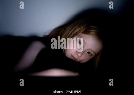 Low-light portrait of a girl using a screen at night, with blue light reflecting on her face. Stock Photo