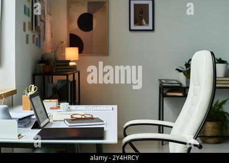 Modern office interior featuring organized desk with laptop, stationery, and plants while having minimalistic design and cozy atmosphere enhancing productivity Stock Photo