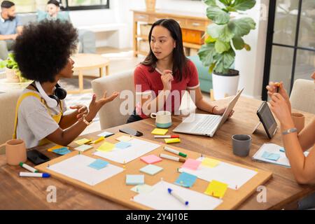 Collaborating on project, young friends using laptop and sticky notes at table, start up business Stock Photo