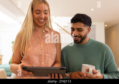 Smiling friends using tablet and drinking coffee, enjoying time together indoors Stock Photo