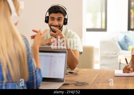 Using laptop and wearing headphones, man smiling and talking with friends Stock Photo