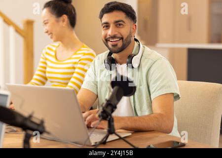 Smiling man using laptop with headphones and microphone, working from home Stock Photo