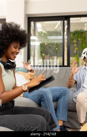 Using tablet and wearing headphones, young woman enjoying time with diverse friends Stock Photo