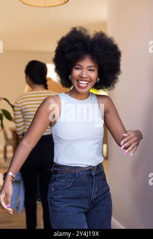 Smiling young woman with afro hairstyle walking indoors, enjoying time with friends Stock Photo