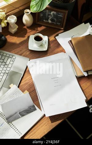 Papers, notebooks, and a hot coffee placed on a wooden desk near laptop and window, suggesting focused work and productivity in office environment Stock Photo