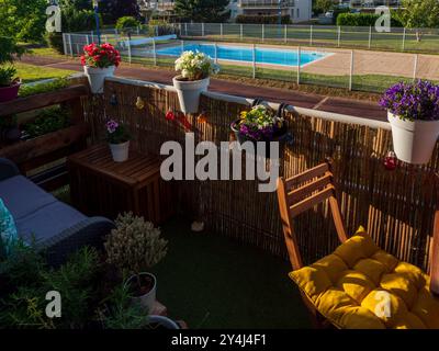 balcony in flowers at sunset, table with wooden chairs, place to relax, swimming pool in the background Stock Photo