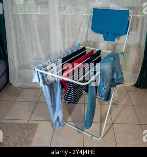 drying laundry at home, hanging clothes on a dryer next to the window, problem of drying in apartments during bad weather Stock Photo