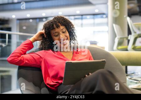 Smiling businesswoman using tablet while sitting in modern office lounge area Stock Photo