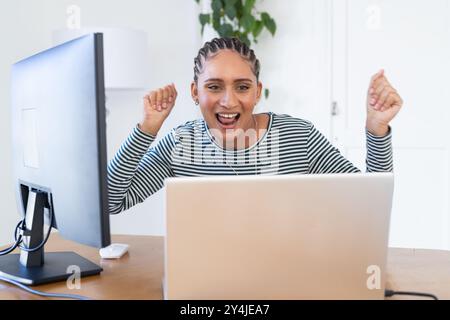 Celebrating success, woman using laptop and desktop computer at home office Stock Photo