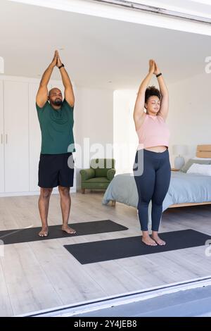 Practicing yoga, man and woman with curly hair stretching on yoga mats in bedroom Stock Photo