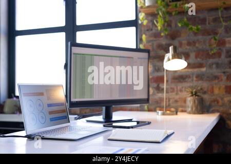 Working on business analytics, laptop and monitor displaying data in office Stock Photo