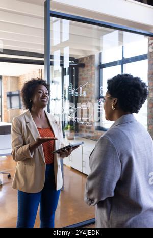 Discussing business strategy, two women collaborating in modern office with tablet Stock Photo