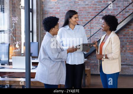 Discussing project, three businesswomen collaborating in modern office with tablet Stock Photo