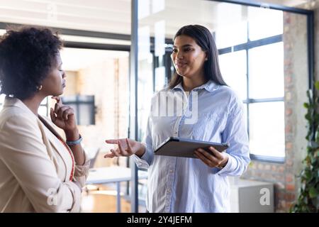 Businesswoman holding tablet, discussing project with colleague in modern office Stock Photo