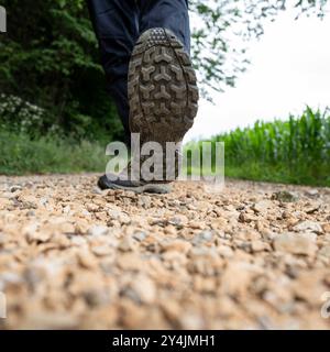 Low angle view of male legs with hiking shoes stepping towards the camera on a gravel trail in nature. Conceptual image of hiking and taking on a jour Stock Photo