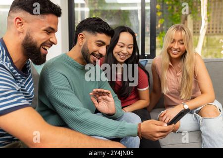 diverse friends sitting on couch, smiling and looking at smartphone together Stock Photo