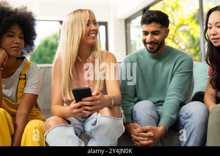 diverse friends sitting on couch, smiling and using smartphone, enjoying time together Stock Photo
