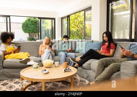 diverse friends sitting on couch using smartphones and relaxing in living room, copy space Stock Photo