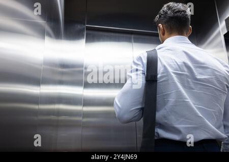 Businessman with shoulder bag standing in elevator, commuting to work, copy space Stock Photo