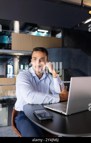 Working in modern office, man using laptop and smartphone, looking thoughtful Stock Photo
