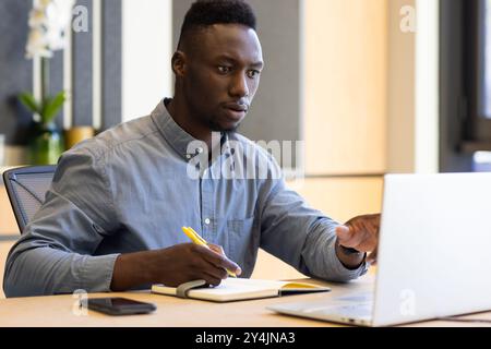 Working on laptop, man taking notes in office, focusing on task Stock Photo