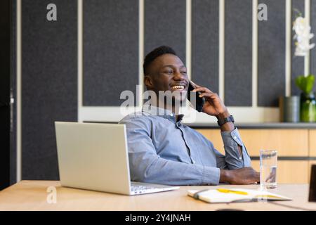 Talking on smartphone, man smiling and working on laptop at office desk Stock Photo