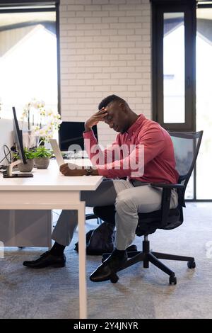 Stressed businessman sitting at desk, looking at tablet in modern office Stock Photo