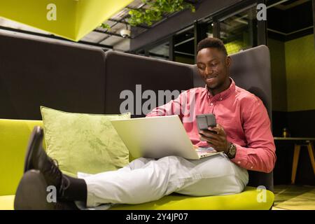Using smartphone and laptop, man working remotely in modern office lounge Stock Photo