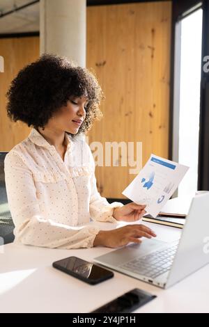 Analyzing business report, woman using laptop and holding document in office Stock Photo