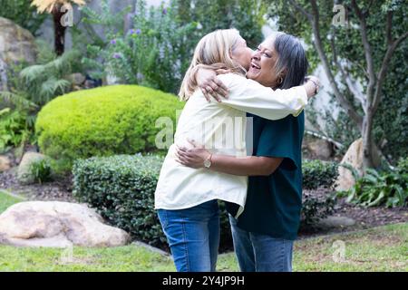 In garden, hugging and laughing, two senior multiracial female friends enjoying time together Stock Photo