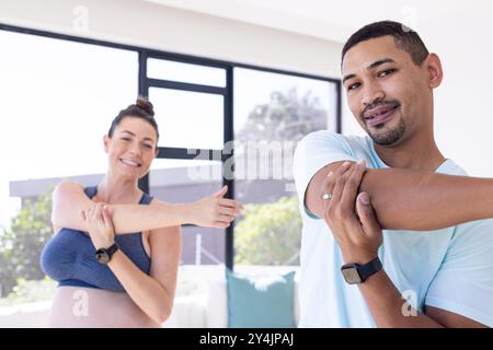 Multiracial couple, Stretching together, pregnant woman and man smiling during home workout session Stock Photo